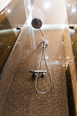 Naklejka na ściany i meble Shower head in brown shower cubicle. Bottom view, brown mosaic wall.