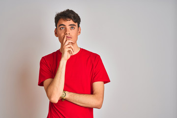 Teenager boy wearing red t-shirt over white isolated background with hand on chin thinking about...