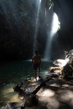  Backside of man traveler stand under the ray of light in the cave. Form Bali. Travel concept. The Gitgit waterfall on the island of Bali. Waterfall in the tropical forest.