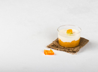 Vanilla Panna cotta in a glass Cup, Italian dessert creamy jelly with a tangerine layer, decorated with pieces of Mandarin and kiwi on a light background