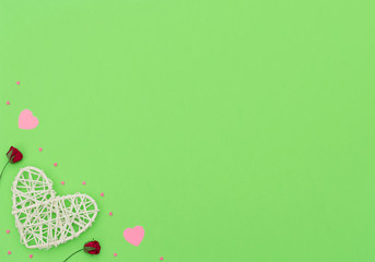 Valentine's Day green background with rattan and paper hearts, red roses and small pink hearts. Greeting, invitation card. Wedding, love, happiness concept. Flat lay, top view with copy space.
