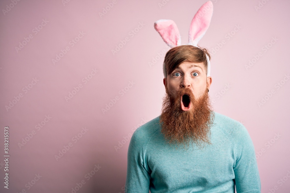 Sticker Hipster Irish man with beard wearing easter rabbit ears over isolated pink background afraid and shocked with surprise expression, fear and excited face.