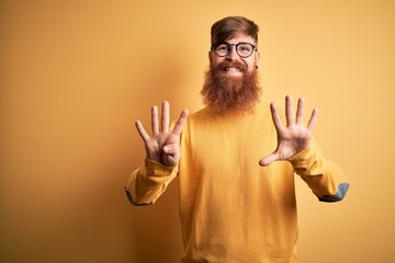 Handsome Irish redhead man with beard wearing glasses over yellow isolated background showing and...