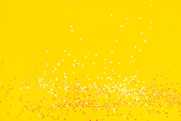 Tiny pearl stars on yellow background. Flat lay, top view.
