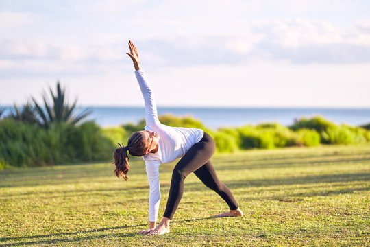 Young beautiful sportwoman practicing yoga. Coach teaching revolved triangle pose at park