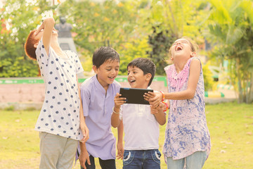 Group of Children laughing by seeing media on mobile - kids having fun by by looking on Smartphone - concept of teens addicted to cellphones and technology.