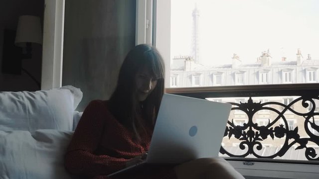 Happy beautiful European business woman using laptop mobile office on cozy French balcony bed on vacation slow motion.