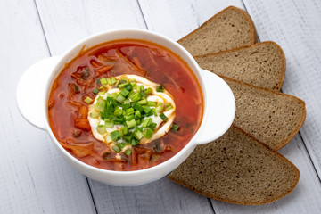 Ukrainian red borsch with sour cream in white plate and pieces of dark brown bread. Russian cuisine concept. Light wooden background.