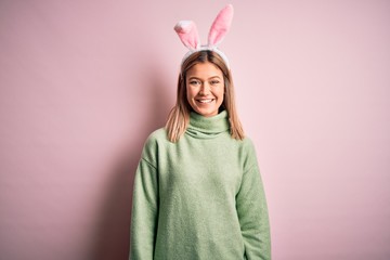 Young beautiful woman wearing easter rabbit ears standing over isolated pink background with a happy and cool smile on face. Lucky person.