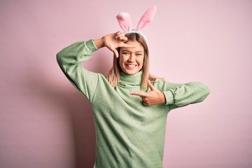 Young beautiful woman wearing easter rabbit ears standing over isolated pink background smiling making frame with hands and fingers with happy face. Creativity and photography concept.