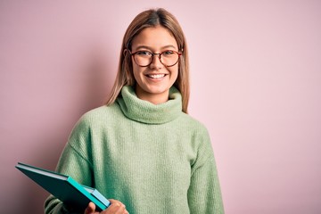 Young beautiful woman wearing glasses holding books over isolated pink background with a happy face...