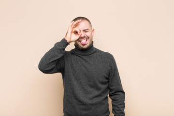 young handsome man smiling happily with funny face, joking and looking through peephole, spying on...