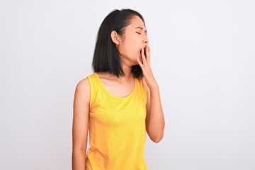 Young chinese woman wearing yellow casual t-shirt standing over isolated white background bored yawning tired covering mouth with hand. Restless and sleepiness.