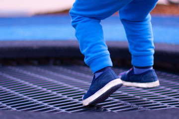 A boy on the playground jumping on a trampoline. A view of legs hovering in the air.