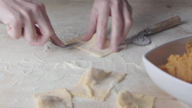 Closeup process making ravioli vegan homemade pasta. Housewife cook closes with a fork 'tortelli di zucca', traditional italian pasta, woman cooking food on kitchen