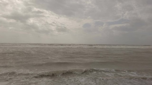 Stormy evening at the beach with rough sea splashing on the shore, a lot of foam water,  and overcast sky with dramatic light