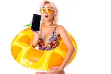Pretty blonde caucasian female stands in swimsuit with rubber beach pineapple ring and shows a...