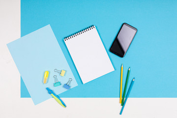 Mobile phone and different stationery isolated on whitte and blue background