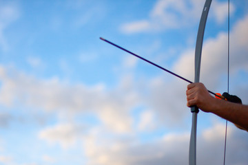 Archer's hands stretching bow and arrow pointing up in nature against the sky
