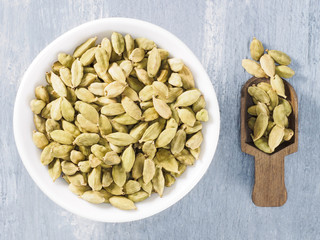 Spice green cardamom (Elettaria cardamomum) in a ceramic white bowl with wooden scoop. Modern apothecary, naturopathy and ayurveda concept
