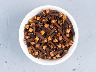 Cloves spice in a white bowl on a gray concrete background