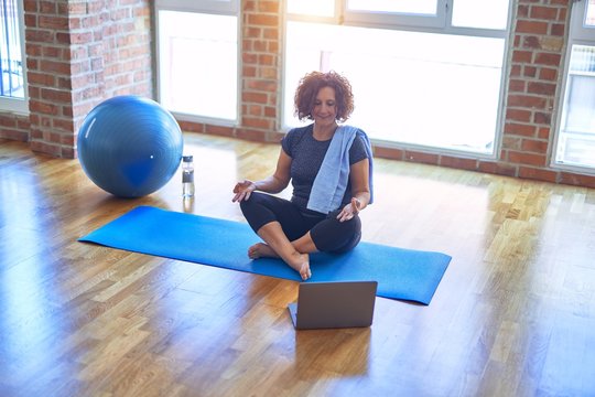 Middle age beautiful sportswoman smilig happy. Sitting on mat with smile on face using laptop at home