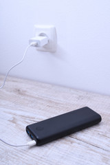 Black phone power bank plugged in the socket on the wall for charging on wooden background