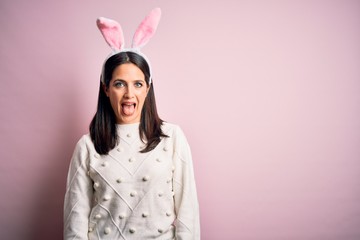 Young caucasian woman wearing cute easter rabbit ears over pink isolated background sticking tongue out happy with funny expression. Emotion concept.