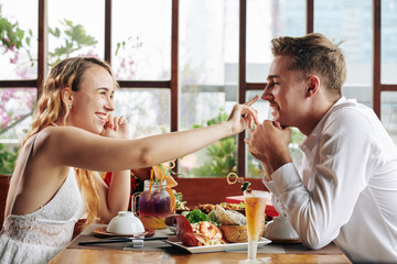 Horizontal side view shot of young woman touchng her boyfriend's nose with her finger on date in cafe