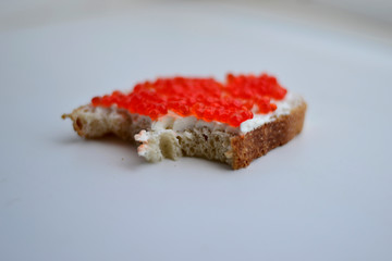 Bitten sandwich with curd cheese and red caviar on a white background
