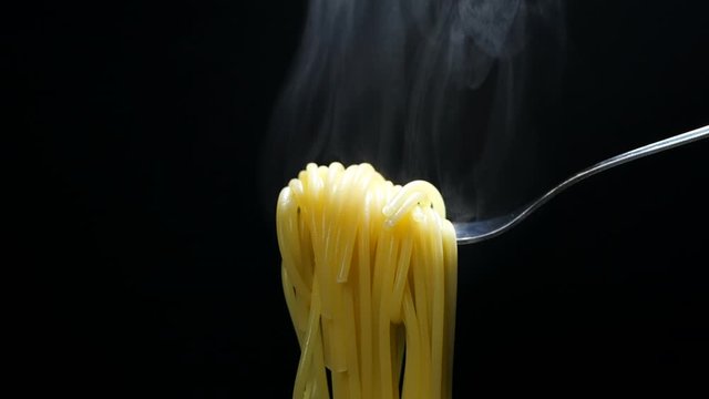 Spaghetti on black background. Spaghetti on fork with steam in slow motion