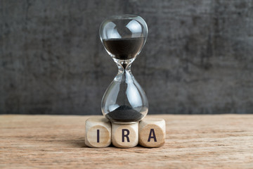 Sandglass or hourglass with black sand falling on cube wooden block with alphabet buiding the word IRA using as Individual Retirement Account concept