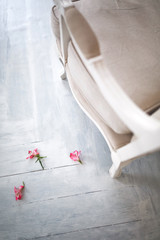 Fototapeta na wymiar Pink flowers are scattered on the wooden floor by a beautiful light colored chair. Vintage interior design.