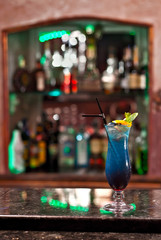 Blue cocktail on the bar counter. Drink with martini, gin, rum, tequila and fruit on the background of bottles with alcohol. Glass with booze on a marble board.