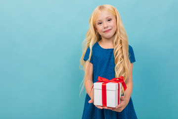 cute blond child in a dress with a gift in his hands on a light blue background with copy space
