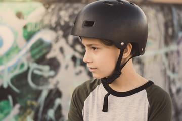 Portrait of trendy young skater at the skatepark wearing helmet, looking away. Smiling teenager enjoying sunny day outdoors in the city with skateboard. Youth, health, safety, sport, positive concept