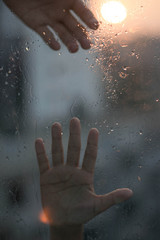 Two hands is trying to reach each other on a raindrop window