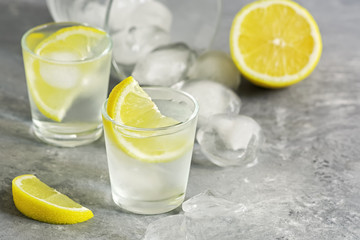 Vodka shot glass with ice and juicy lemon slices on a gray concrete background. Traditional Russian alcohol. Selective focus, copy space.