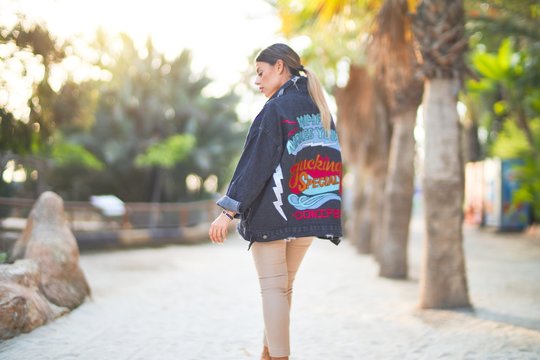 Young beautiful woman wearing denim jacket standing backwards at the town park