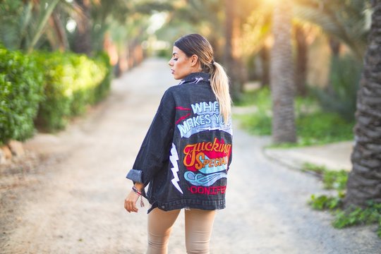 Young beautiful woman wearing denim jacket standing backwards at the town park