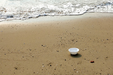 White plastic deep disposable plate on beautiful beach.