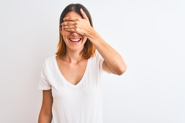 Beautiful redhead woman wearing casual white t-shirt over isolated background smiling and laughing with hand on face covering eyes for surprise. Blind concept.