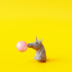 Concrete unicorn statue blowing a chewing gum bubble on yellow background. Creative idea. Minimal concept. 3d rendering