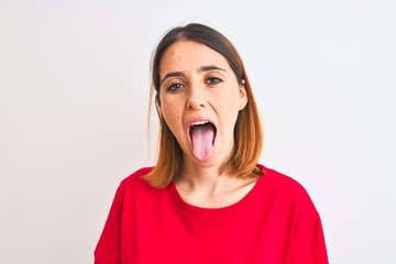 Beautiful redhead woman wearing casual red t-shirt over isolated background sticking tongue out...