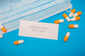 Medical mask, orange and white capsules on a blue background and the inscription coronavirus on a white sheet of close-up. First aid, care during illness. Background