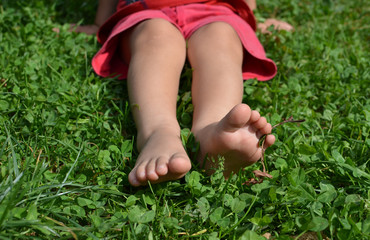 Kid sitting bare footed on the green grass, clover leaves, in red shorts. Child's feet on the grass, toes, happy feeling, warm sunny day, Earth day, Earth contact