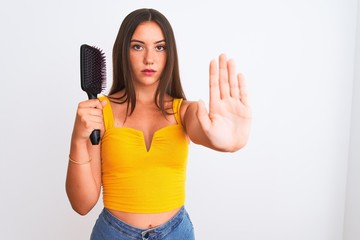 Young beautiful girl holding hair comb standing over isolated white background with open hand doing stop sign with serious and confident expression, defense gesture