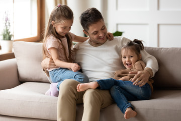 Fototapeta premium Loving father relax cuddle with little daughters on couch
