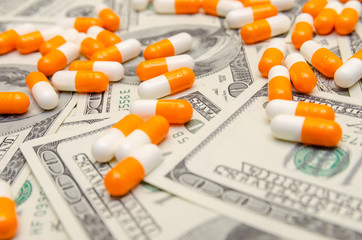 A lot of white and orange tablets on the background of dollar bills close-up. Concept of insurance, medicine