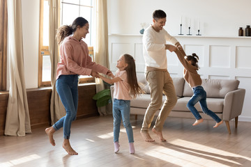 Happy parents dancing with small daughters in living room